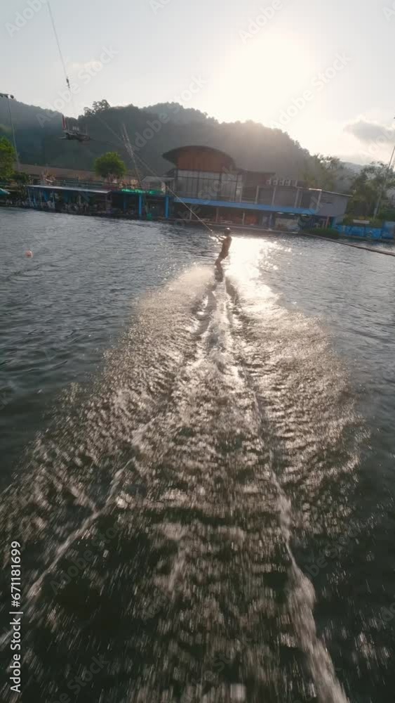 Vertical video 4k. Wakeboarder man ride touch water hand cable