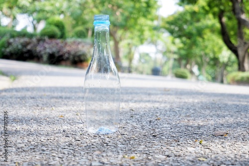 An empty of drinking plastic bottle littering on the ground floor in plubic park road with blurred street background