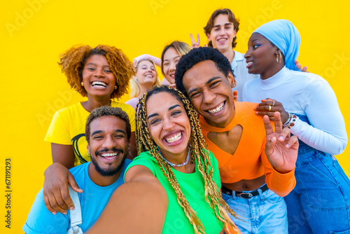 Diverse young people smiling while taking a selfie in a yellow background