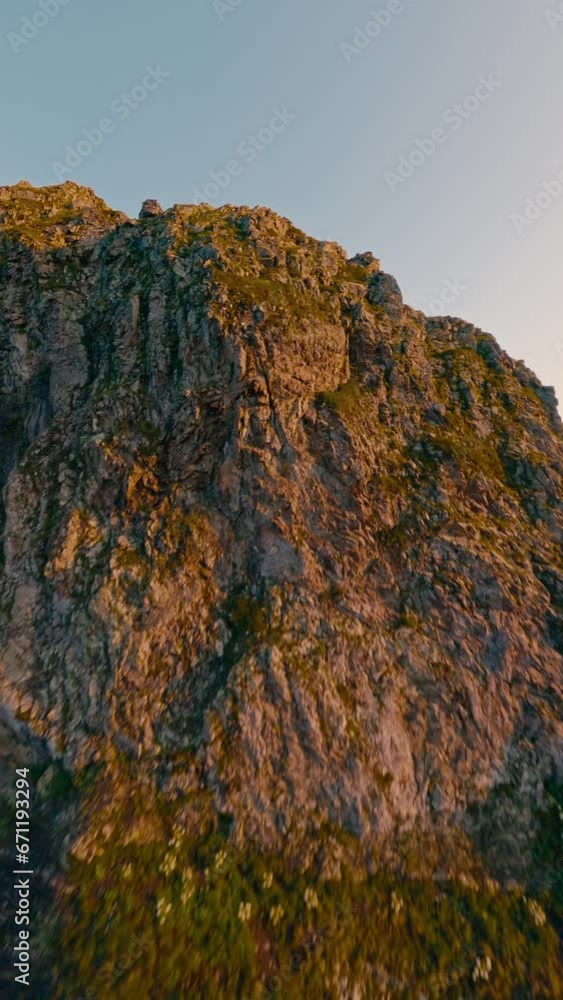 Vertical video 4k. Mountain summit geology formation rock texture natural sunrise morning sunlight valley landscape aerial view. FPV sport drone shot extreme altitude cliff panorama snow green grass