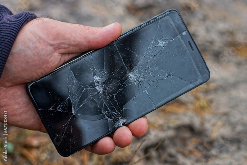 modern new glass broken with cracks black screen of a mobile touch phone in a person's hand on the street during the day
 photo