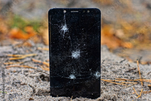 modern new glass broken with cracks black screen of a mobile touch phone in the ground on the street during the day 