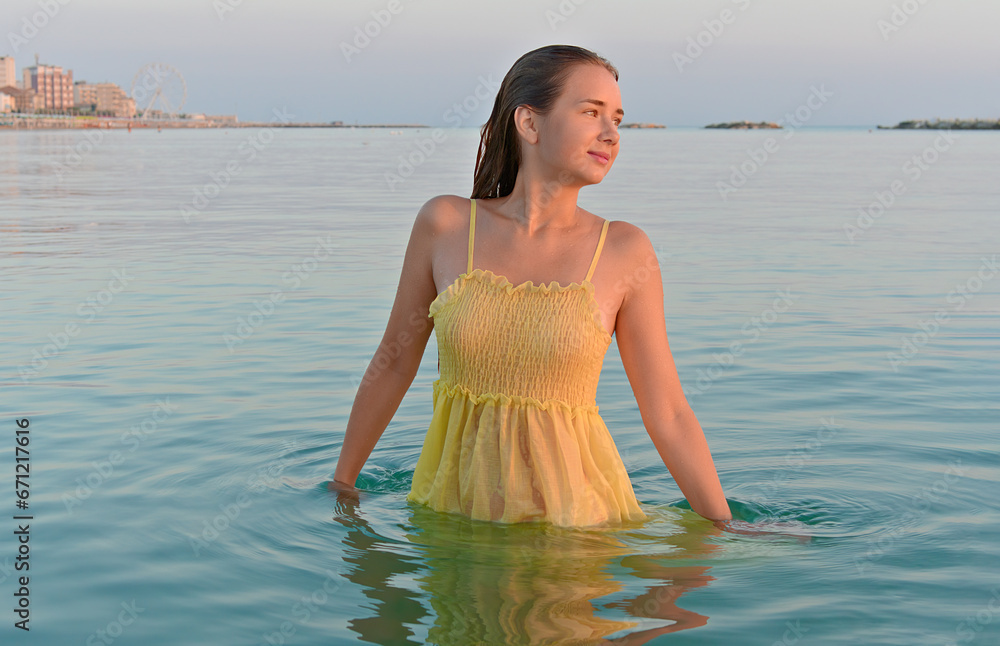 Young woman in a yellow dress under sunrise on the seashore against the backdrop of the city Young woman in a yellow dress under sunrise on the seashore against the backdrop of the city