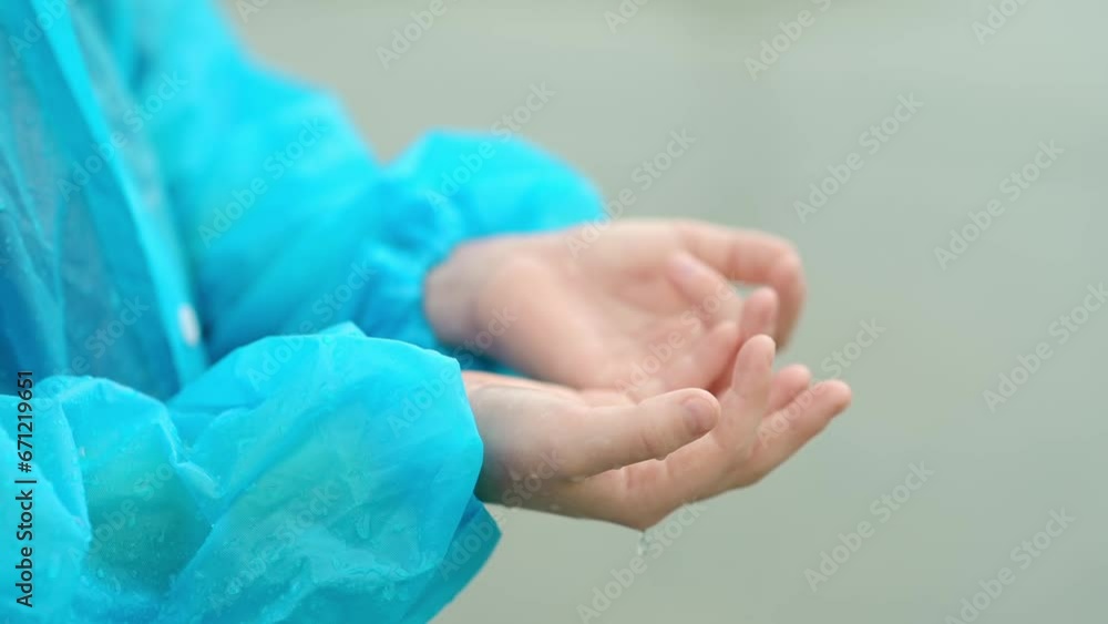 Close-up of a child's hands in the pouring rain. A joyful boy in a blue raincoat tries to catch raindrops in his palms while walking on a rainy day. Children love to run and play in rainy weather Close-up of a child's hands in the pouring rain. A joyful boy in a blue raincoat tries to catch raindrops in his palms while walking on a rainy day. Children love to run and play in rainy weather