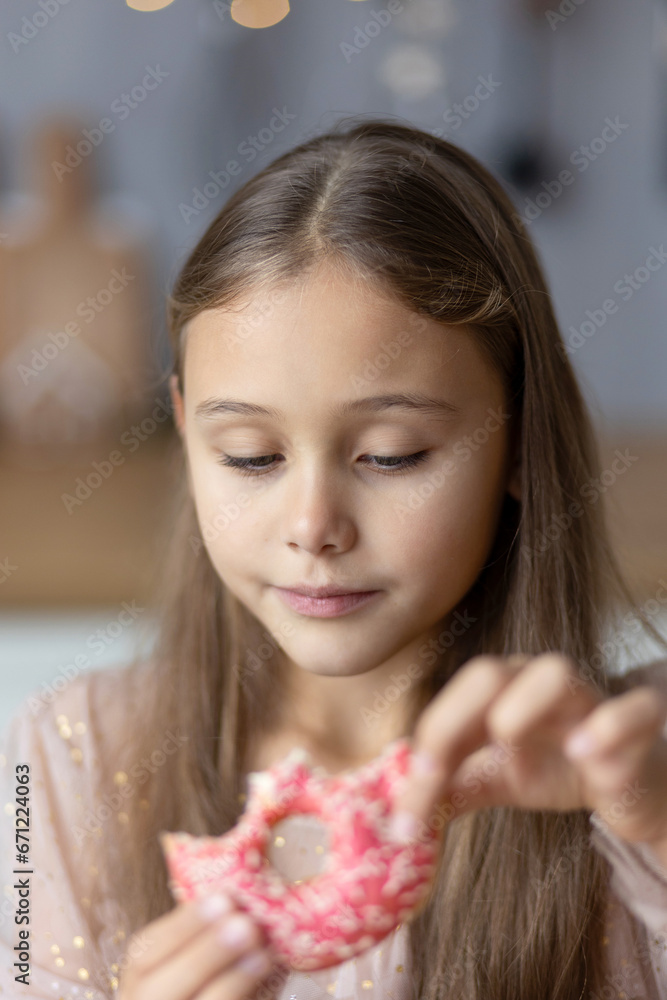 Little happy girl with long hair playing and tasting donuts with pink icing at kitchen Little happy girl with long hair playing and tasting donuts with pink icing at kitchen