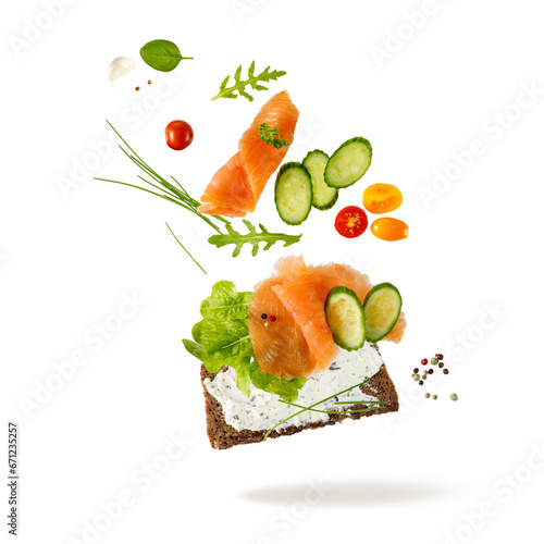 Smoked salted salmon filet with vegetables and herbs falling on slice of rye bread isolated on white background.