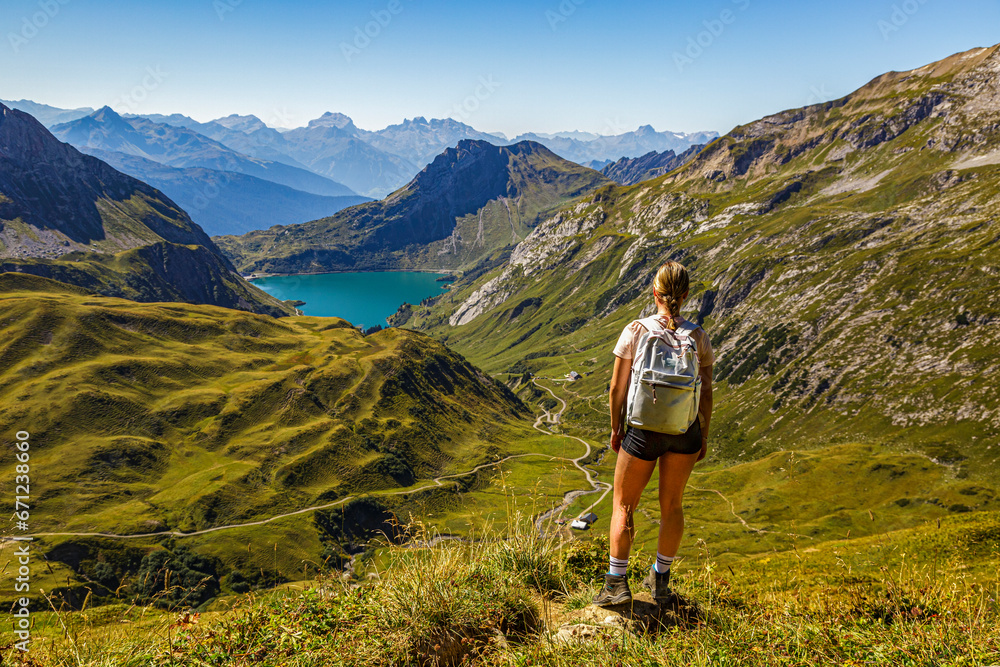 eine junge Frau steht an einem Wanderweg auf einem Berg und schaut auf den Spullersee in Vorarlberg Lech Östereich
