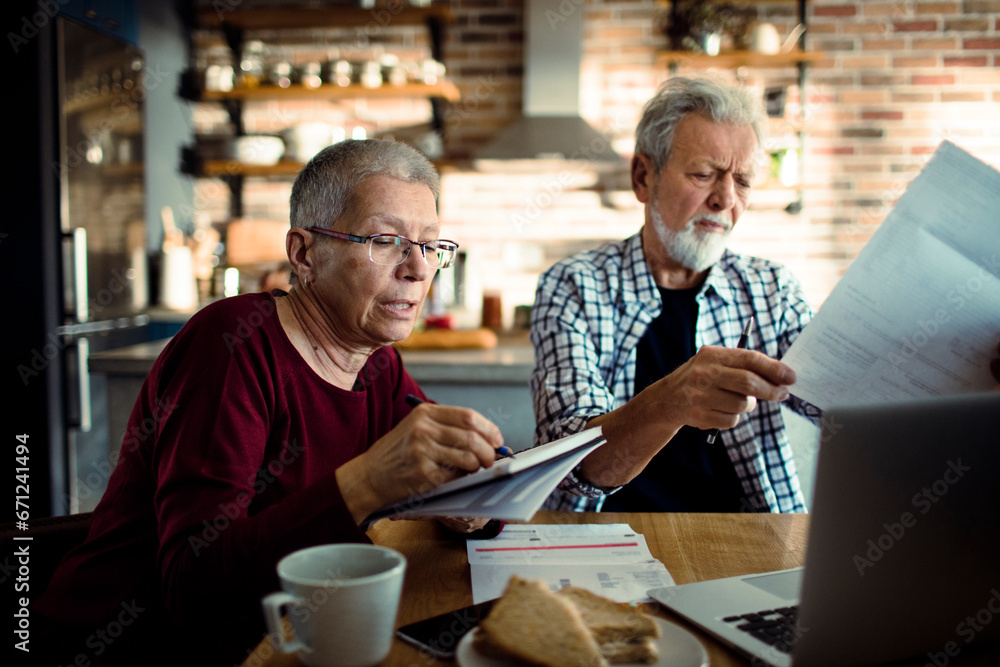 Senior couple doing bills and payments together in the kitchen at home Senior couple doing bills and payments together in the kitchen at home