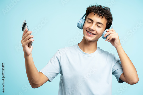 Portrait of smiling teenage boy wearing headphones listening to music, holding mobile phone