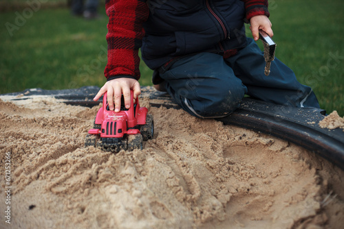 Close up photography of a boy playing with his plastic red tractor in an outdoor sandpit