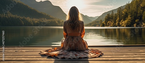 A girl of Caucasian descent is sitting on a dock made of wood which is located above a lake photo