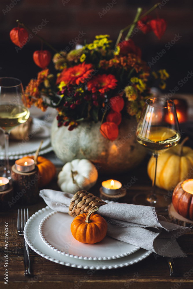 Beautiful elegant table setting for candlelight Thanksgiving Day dinner or Halloween party at home. Fancy dishware, porcelain plates. Floral centrepiece, pumpkins and burning candles as decor