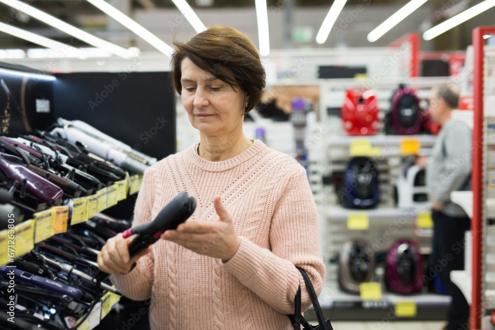 Middle aged caucasian woman choosing hair iron in appliance store.