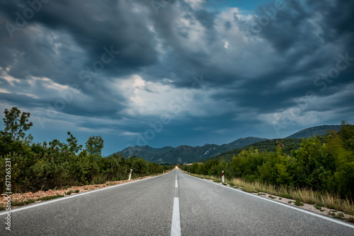 Asphalt road panorama in countryside on cloudy day. Road in forest under dramatic cloudy sky. Image of wide open prairie with a paved highway stretching out as far as the eye can see.