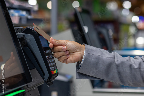 Close-up photo of the hand of a female buyer paying in a supermarket store with a bank credit card at the self-service checkout.