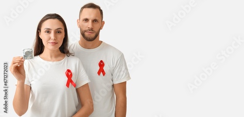Young couple with red awareness ribbons and condom on light background with space for text. Banner for World AIDS Day