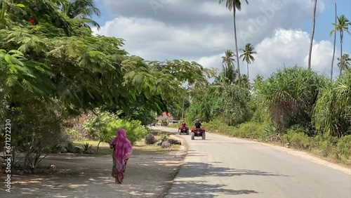 Quad biking on dusty African roads along a palm tree alley on a clear sunny day
