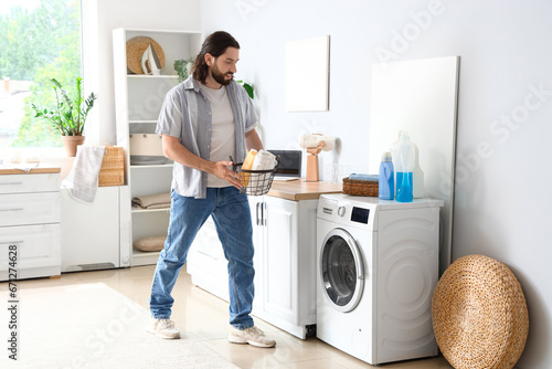 Young man with laundry basket near washing machine at home