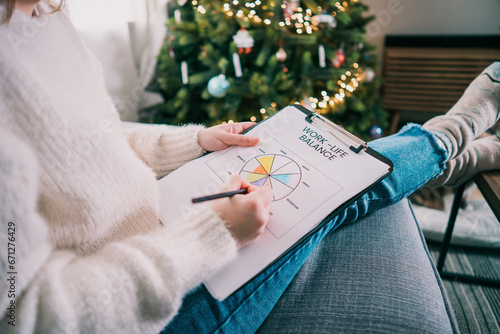 Woman drawing work-life balance wheel sitting on the sofa at home. Self-reflection and life planning for next new year. Personal Year review. Coaching tools. Finding Balance in Life. Selective focus.