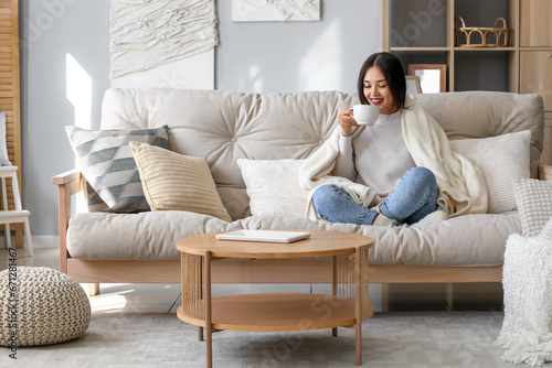Young Asian woman with warm plaid drinking tea at home