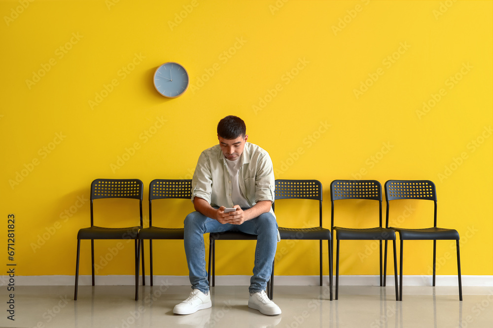 Young man with mobile phone waiting for his turn in room - obrazy, fototapety, plakaty 