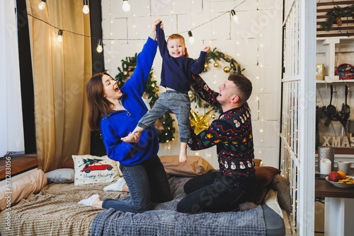 Happy family couple at home with child in New Year locations. New Year's festive mood in the family circle. Christmas decorations in the bedroom. New Year at home. Christmas decorations at home