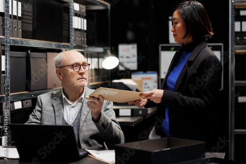Senior private detective receiving criminal case investigation file from asian assistant coworker. Teamwork and cooperation in criminology agency file cabinet office room © DC Studio