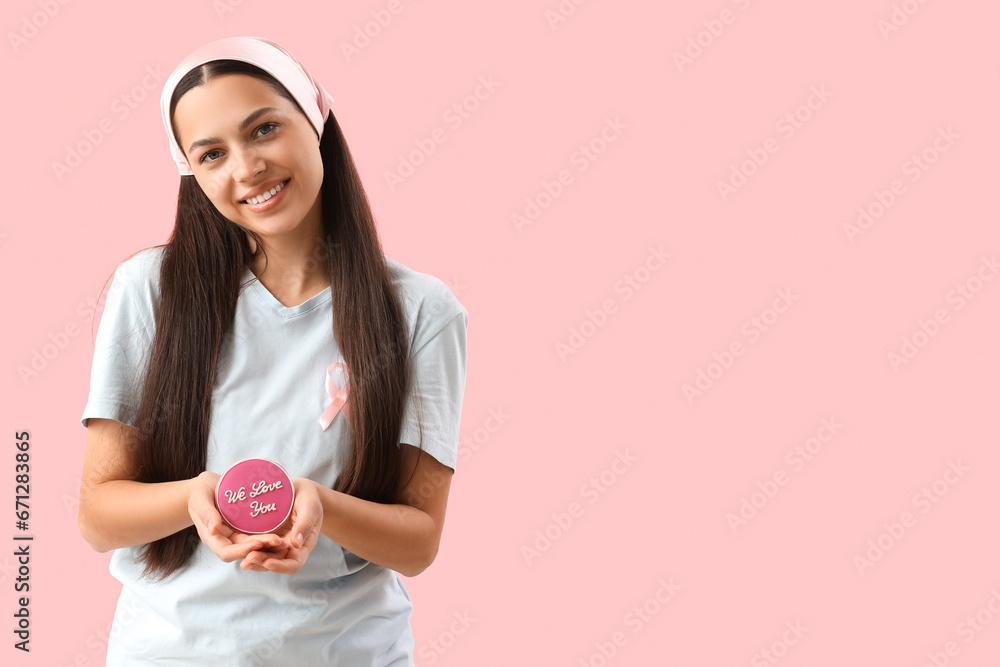 Young woman holding cookie with text WE LOVE YOU on pink background. Breast cancer awareness concept Young woman holding cookie with text WE LOVE YOU on pink background. Breast cancer awareness concept