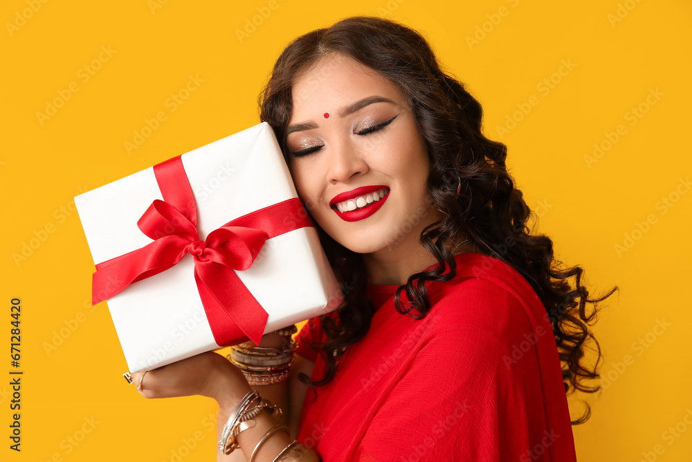 Beautiful Indian woman in sari with gift box on yellow background Beautiful Indian woman in sari with gift box on yellow background