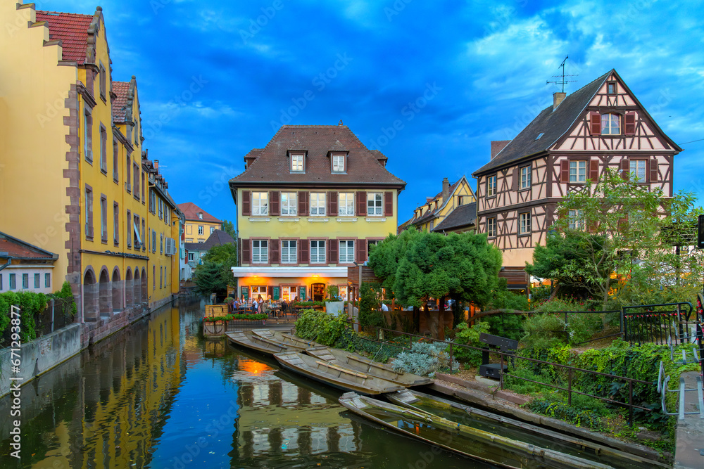 Twilight evening views of half timbered buildings and illuminated waterfront cafes on the Lauch River in the historic medieval Little Venice district of Colmar, France, in the Alsace region.	
