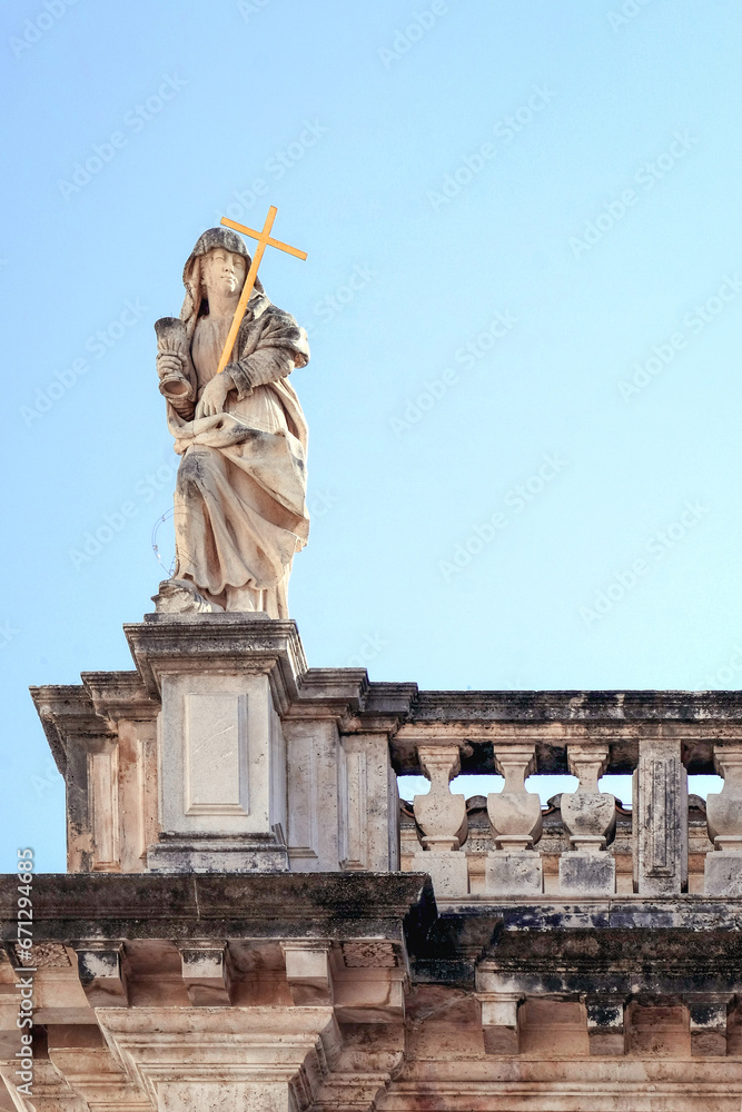 Sculpture of a saint holding a gold cross on the facade of the Church of St. Vlach on Stradun Street in the city of Dubrovnik.