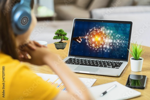 Joven mujer trabajando en su laptop. Rodeada con sus plantas en su escritorio. Utiliza auriculares. Observa en su computador una red de gente conectada. Muchos contactos. Toma nota. Tiene su móvil.