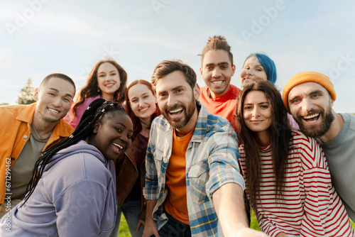 Group of smiling multiracial friends wearing colorful casual clothing taking selfie in green park. Happy attractive men and women communication, standing together outdoors. Diversity, friendship  © Maria Vitkovska