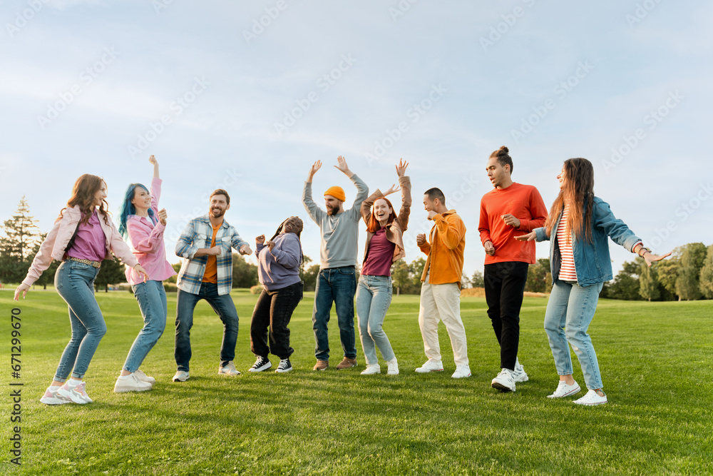 Big group of happy stylish multiracial friends wearing colorful clothing dancing on corporate party in park. Diversity, friendship, positive lifestyle  concept   