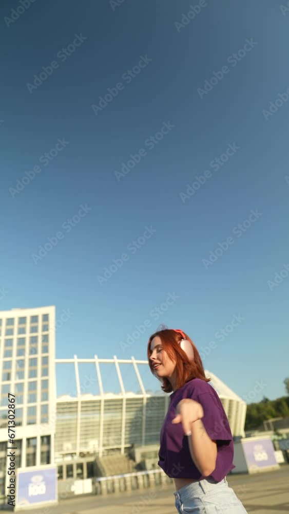 The stunning red-haired woman, with headphones on, is dancing in the city center square. The stunning red-haired woman, with headphones on, is dancing in the city center square.