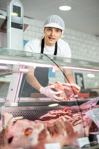 Male meat vendor provides selection of fresh, organic options at grocery store.