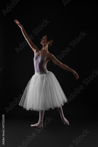 Young ballerina practicing dance moves on black background