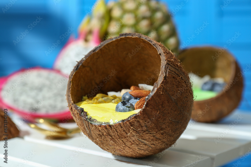 Tasty smoothie bowl with fresh blueberries and almonds served in coconut shell on white wooden table, closeup