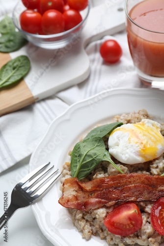 Delicious boiled oatmeal with poached egg, bacon and tomato served on table, closeup