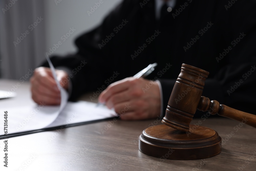 Judge with gavel writing in papers at wooden table, closeup