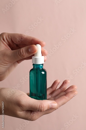 Woman with bottle of cosmetic serum on light pink background, closeup