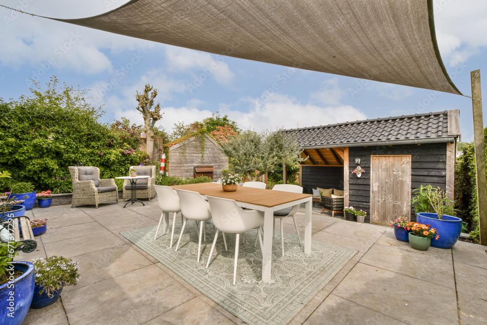 a patio area with chairs, tables and an umbrella over the dining table in front of a wooden shed behind