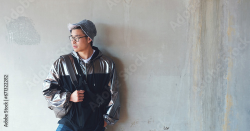 Fashion, student and gen z asian male streetwear, style and cool clothes on wall background, confident and chilling. Travel, fashionable and Japanese guy outdoors casual, contemporary and stylish