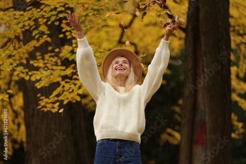 Autumn vibes. Happy woman throwing leaves up in park