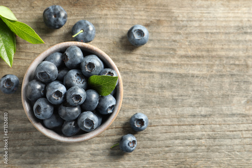 Bowl of tasty fresh blueberries with leaves on wooden table, flat lay. Space for text