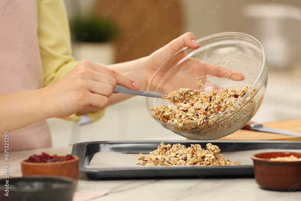 Making granola. Woman putting mixture of oat flakes, dried fruits and other ingredients onto baking tray at light table, closeup Making granola. Woman putting mixture of oat flakes, dried fruits and other ingredients onto baking tray at light table, closeup