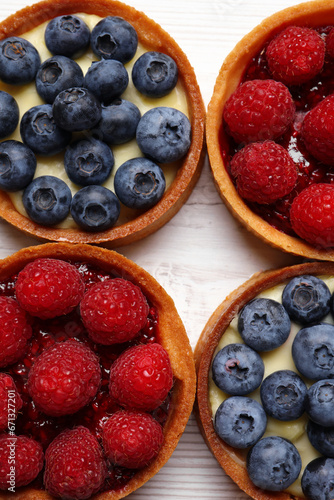 Tartlets with different fresh berries on white wooden table, flat lay. Delicious dessert