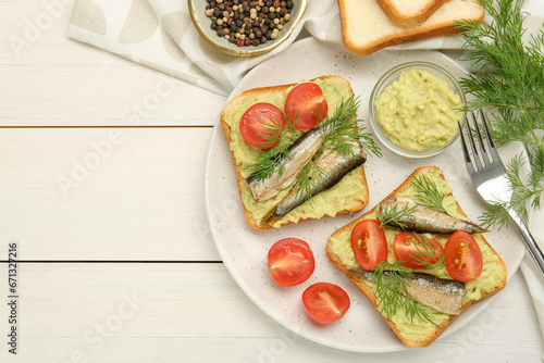 Delicious sandwiches with sprats, tomatoes, dill and avocado puree served on white wooden table, flat lay. Space for text