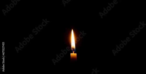 A single burning candle flame or light glowing on an orange candle on black or dark background on table in church for Christmas, funeral or memorial service with copy space.