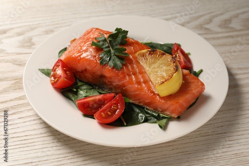 Tasty grilled salmon with tomatoes, lemon and basil on white wooden table, closeup